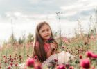 portrait of a little beautiful girl sitting in a clover field at sunset during summer vacation